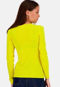 Long-sleeve, bright yellow sweater made of soft knit fabric. Features a fitted design and rounded neckline, paired with dark denim.