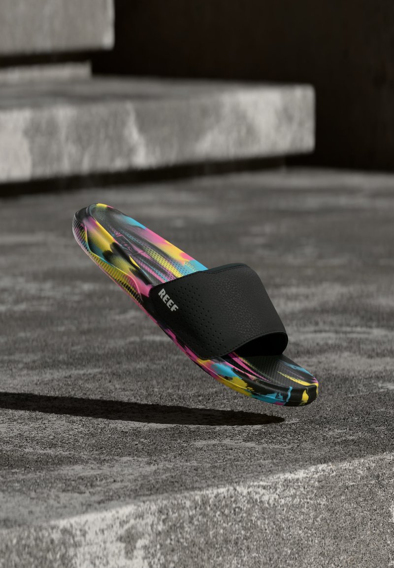 Sandale à enfiler avec sangle noire et semelle multicolore vibrante flottant au-dessus des marches en béton.