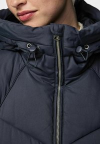 Námorně modrá prošívaná bunda s vysokým límcem, nastavitelnými šňůrkami, zipovým zapínáním a diamantovým prošívaným vzorem.