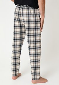 Flannel pajama pants in a beige, black, and white plaid pattern; features an elastic waistband and straight-leg design.