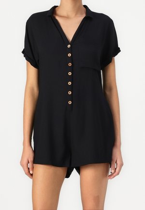 Black short-sleeve romper with a collar, eight wooden buttons down the front, one chest pocket, and a loose fit with high side slits.