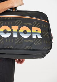 Sort stofpose med iøjnefaldende "VICTOR" skrift i orange, hvid og gul striber. Tekstur overflade med subtile geometriske mønstre.
