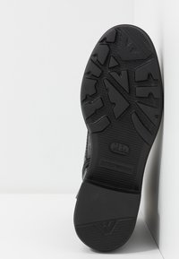 Černé tenisky s texturovanou gumovou podrážkou, která má jedinečný vzor. Obsahují brandování na patě a mají lehký design.