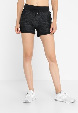 Shorts de sport noirs en tissu texturé, avec une taille élastique et un cordon de serrage réglable. Assortis à des chaussures de sport blanches.
