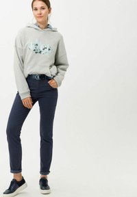 Hoodie gris avec motif graphique, jeans bleu marine avec poignets retroussés et baskets bleu marine. Tissu doux et coupe décontractée. Ceinture en acier inoxydable simple.