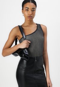Body negru cu fante asimetrice, purtat cu o geantă din piele patentată neagră. Modelul poartă o fustă din piele neagră, mulată.
