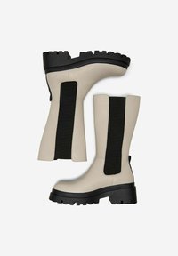 Stivaletti beige alla caviglia con pannelli elasticizzati neri ai lati, suola nera spessa, texture liscia e design a punta arrotondata.