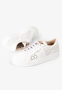Zapatillas blancas perforadas con puntera de cuero suave, cordones blancos planos y un forro interior en un tono marrón claro. Presenta una suela texturizada.