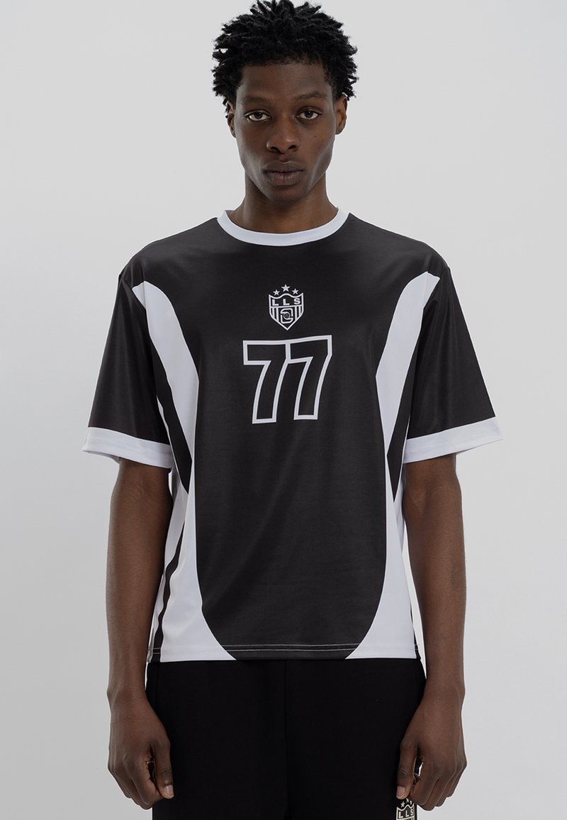 Camisa desportiva de manga curta em preto e branco, com gola redonda, impressão grande do número "77" e logótipo no peito. Tecido suave com design contrastante.