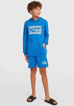 Blå hættetrøje med kængurulomme og hvidt O'Neill-logo, kombineret med matchende blå shorts. Sorte slidesandaler fuldender outfittet.