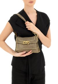 Borsa a mano in pelle grigia con borchie dorate, forma rettangolare, chiusura a patta e tracolla regolabile, tenuta davanti da una modella.