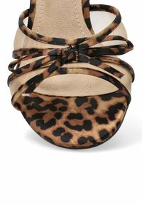 Sandalia de tacón alto con estampado de leopardo, tiras de malla beige, punta afilada y una suela suave y texturizada. Presenta un detalle anudado en la parte frontal.