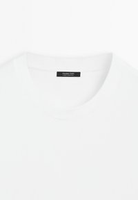 Wit T-shirt met ronde hals en een zwart etiket met "Massimo Dutti Made in Portugal" aan de binnenkant van de kraag, weergegeven op een witte achtergrond.