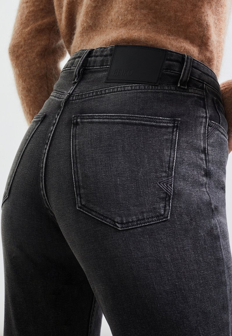 Personne portant un jean noir délavé taille haute et un pull marron duveteux, montrant la poche arrière et la zone de la ceinture.