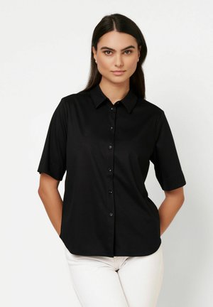 Schwarze kurzärmelige Bluse mit Knöpfen, Kragen, glatter Textur und Knopfleiste vorne. Getragen mit weißer Hose.