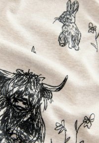 Tela de algodón con ilustraciones negras de una vaca de pelo largo, un conejo y flores sobre un fondo beige claro. Textura suave con sutiles arrugas.
