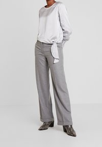 Zilveren satijnen blouse met lange mouwen en een zijstrik, gecombineerd met grijze wijde, gestructureerde broek en puntige slangenprint hakken.