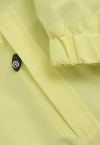 Gul vattentålig tyg med detaljer av vikt cuffs. Har en svart tryckknapp och precisionssömmar som betonar hållbarhet och funktionalitet.