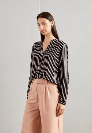 Black and white striped button-up shirt with a v-neck; paired with light pink high-waisted trousers. Smooth fabric, relaxed fit.