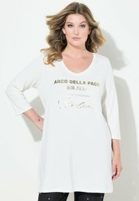 Weiße Langarm-Tunika mit weitem Ausschnitt und metallisch goldener Schriftzug "ARCO DELLA PACE MILANO" auf der Brust.