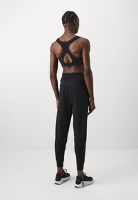 Svart sports BH med nøkkelhull detalj, kombinert med svarte avsmalnende sweatpants og svarte treningssko, sett fra baksiden.