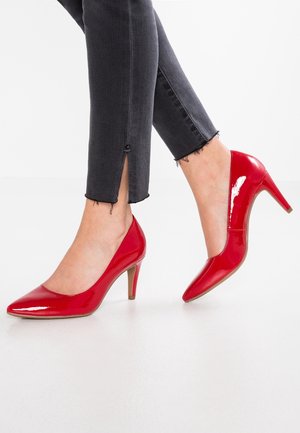 Røde patenterede læderhøjhælede sko med spids tå og en spidstiletto hæl, suppleret af ankelhøje sorte jeans.