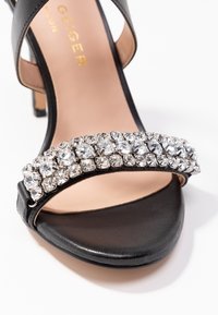 Mustat avonaiset korkokengät, joissa on kaksi riviä kirkkaita strassikiviä etuosan nauhassa ja ohut nilkkaremmi.