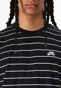 Schwarz-weiß gestreiftes T-Shirt mit kurzen Ärmeln, Rundhalsausschnitt und aufgesticktem Nike SB-Logo auf der linken Brust. Weiches Baumwollmaterial.