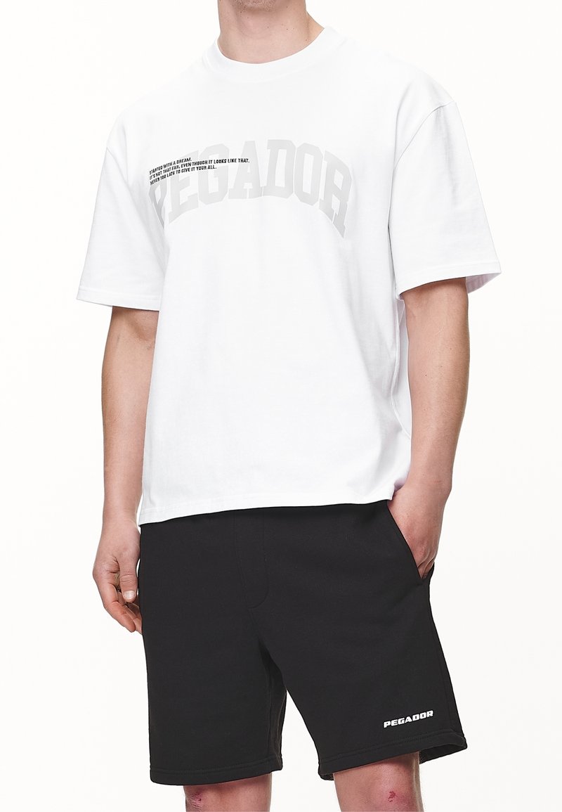 Biała koszulka z bawełny z krótkim rękawem i luźnym krojem, z wyraźnym szarym napisem "PEGADOR" oraz mniejszym czarnym hasłem z przodu.
