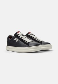 Pair of black leather sneakers with white laces, white soles, and red logo on tongue, shown on white background at slight angle.