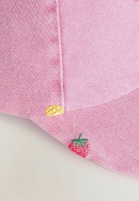Vaaleanpunainen farkkukypärä, jossa on teksturoitu pinta, varustettuna keltaisella brodeeratulla sitruunalla sekä vihreillä ja punaisilla mansikkakoristeilla. Kaareva lippa.