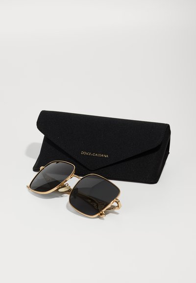 Gafas de sol con montura dorada y lentes oscuros, de forma cuadrada. Acompañadas de una funda de tela negra con letras doradas.