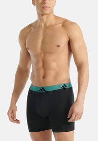 Czarne bokserki wykonane z elastycznego materiału, z miętowym elastycznym pasem z czarnymi akcentami, zaprojektowane dla komfortu i dopasowania.