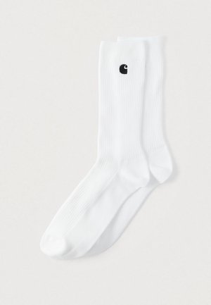 Hvide crew-strømper med ribbet tekstur, med en lille sort logo på siden. Stoffet virker blødt og elastisk.