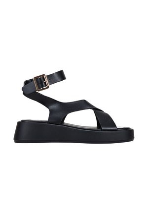 Sandalia de plataforma negra con correa de tobillo ajustable, correas cruzadas, material de cuero suave y una suela gruesa y texturizada.