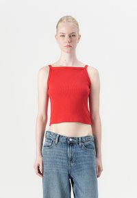 Punainen raidallinen crop-top, jossa on ohuet olkaimet ja neliömäinen pääntie, yhdistettynä korkeavyötäröisiin vaaleansinisiin farkkuihin, joissa on klassinen viiden taskun muotoilu.