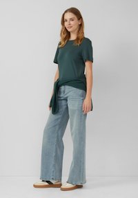 Donkergroen T-shirt met korte mouwen, relaxte pasvorm, gecombineerd met lichtblauwe wijde jeans. Gebreide trui geknoopt om de taille en twee-tonige schoenen.