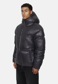Uomo che indossa una giacca invernale imbottita nera lucida con cappuccio, dotata di zip frontale e tasche laterali con zip, in piedi su uno sfondo semplice.