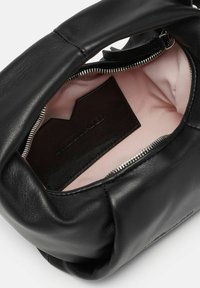 Interno di una borsa a tracolla in pelle nera che mostra un rivestimento rosa chiaro e un'etichetta in pelle scura con testo impresso. Presenta una chiusura con zip.