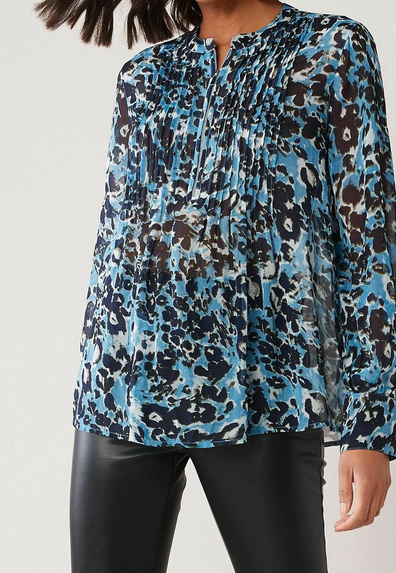 Blusa con stampa leopardata blu e nera, con dettaglio frontale plissettato, scollo rotondo e maniche lunghe, abbinata a pantaloni in pelle nera.