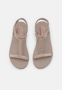 Tan sandals with a textured footbed, a T-strap design, and embellished with horizontal beads and metallic accents. Soft, flexible material.