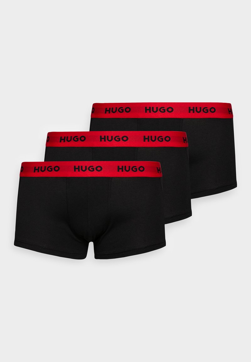 Drei schwarze Boxershorts mit roten elastischen Taillenbändern, die den Markennamen "HUGO" in schwarzer Schrift tragen. Glatte Stofftextur.
