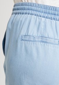 Shorts extensibles bleu clair avec une taille froncée, comprenant une poche arrière et une texture douce et lisse. Design simple sans embellissements.