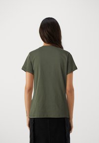 T-shirt en coton vert olive à manches courtes, col rond et coupe décontractée. Porté avec une jupe en denim noir avec des bords effilochés.