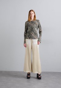 Tricou cu mânecă lungă în dungi zebrate negre și crem, asortat cu pantaloni bej cu picior larg. Pantofii cu platformă au un toc masiv și accent cu fundiță.