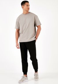 Grå kortærmet t-shirt med rund hals, sammen med sorte tapered joggers. Lyse grå sneakers med hvide accenter. Glat stofstruktur.