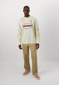 Long-sleeve cream jersey with horizontal stripes and red logo. Paired with beige pants and pink sneakers. Liverpool branding on chest.