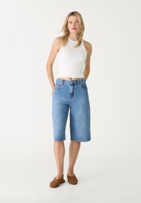 Lyseblå denim Bermuda shorts med lige pasform, fem-lomme-design og frynset kant, parret med en hvid ærmeløs top og brune slip-ons.