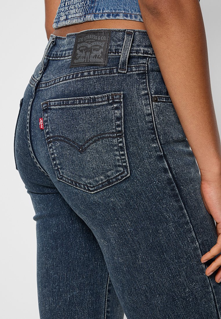 Gros plan sur une personne portant un jean Levi's bleu foncé avec une poche arrière visible, l'étiquette rouge Levi's et une étiquette en cuir sur la ceinture.