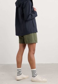Navy waterproof jacket with a hood, olive green shorts, white sneakers, and black-and-white striped socks, shown from a side angle.